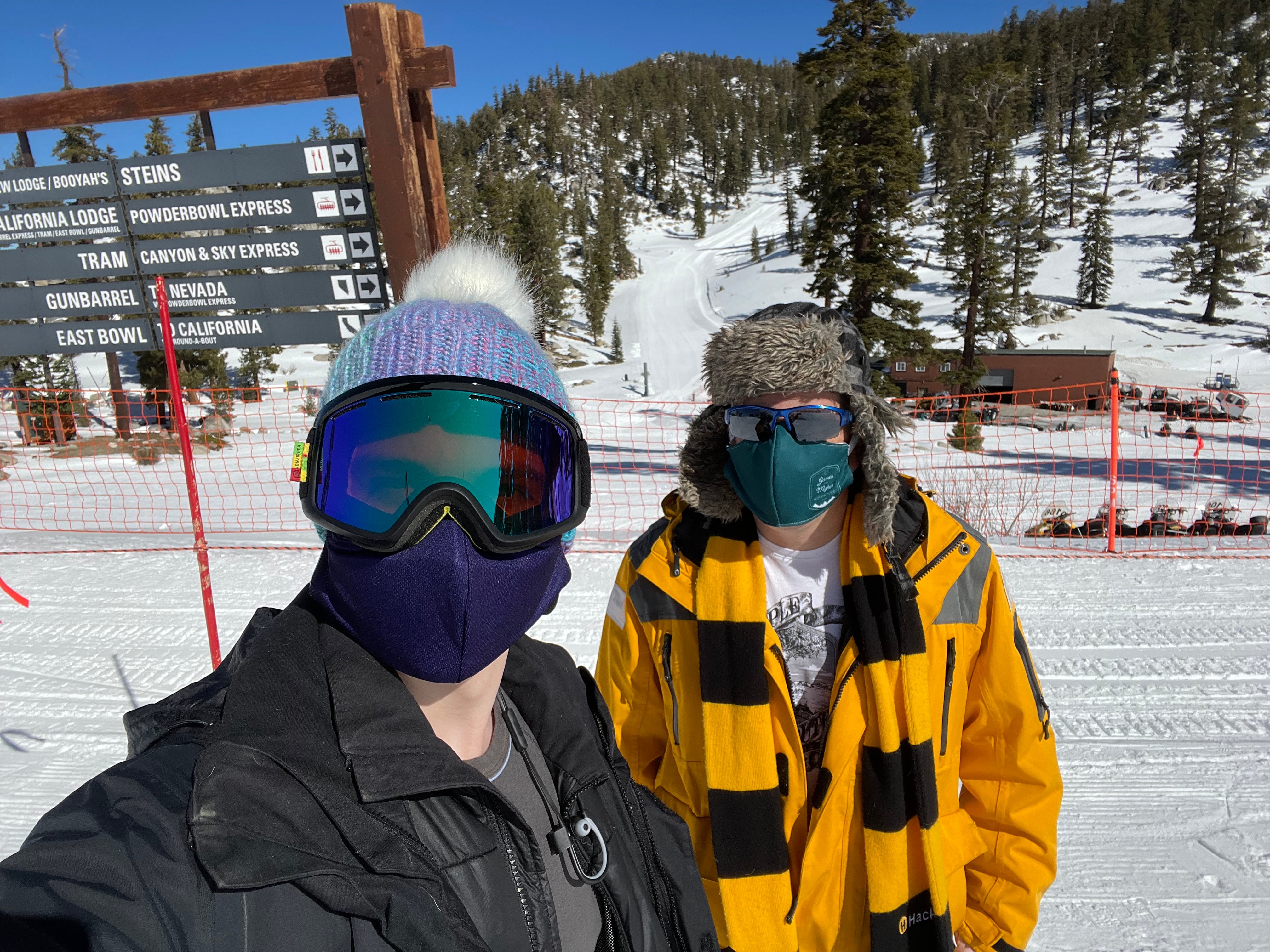 Two men in winter jackets standing in front of signs identifying ski trails.