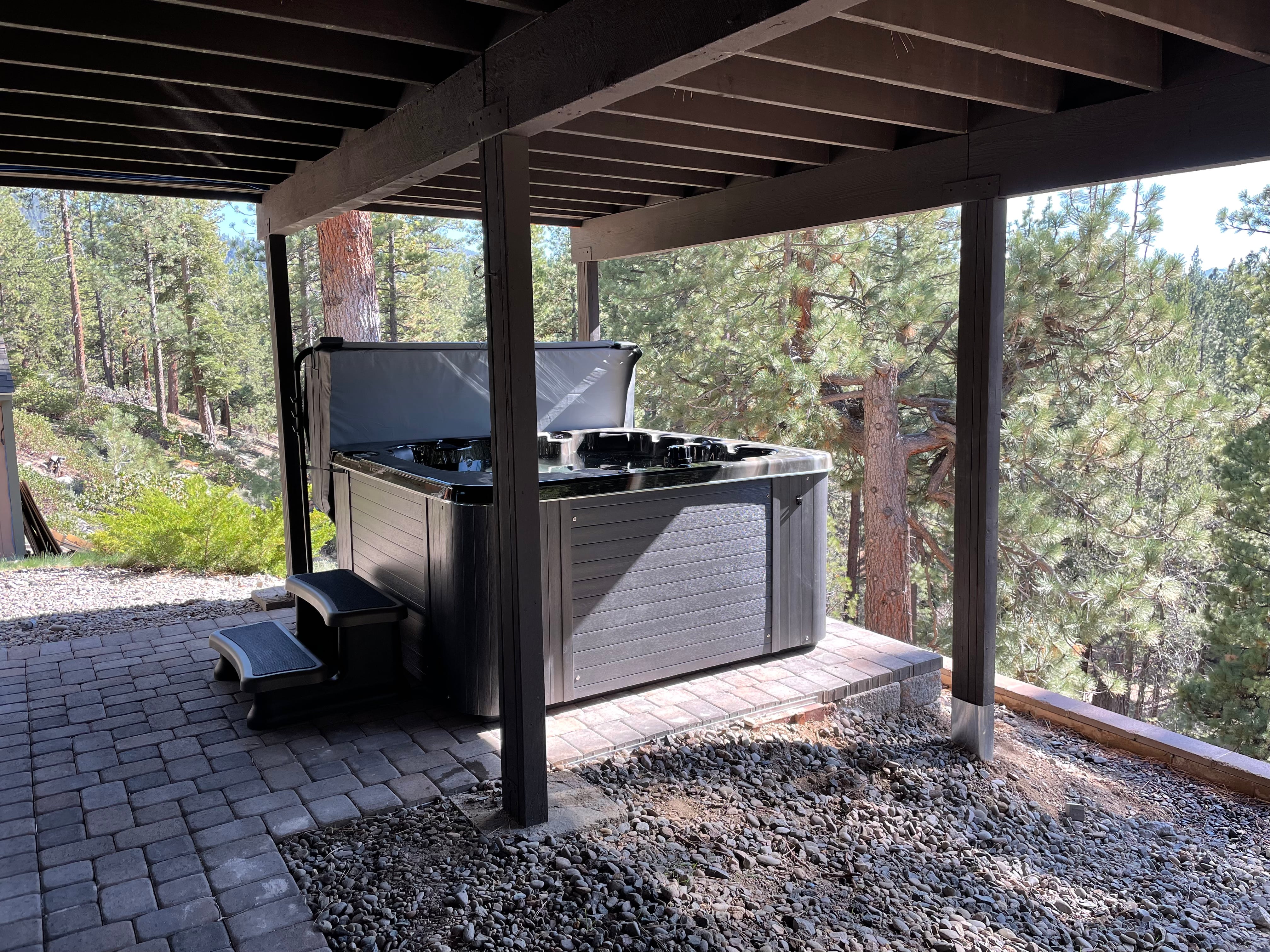 Hot tub installed on a pad made from stone pavers and underneath a wooden deck.