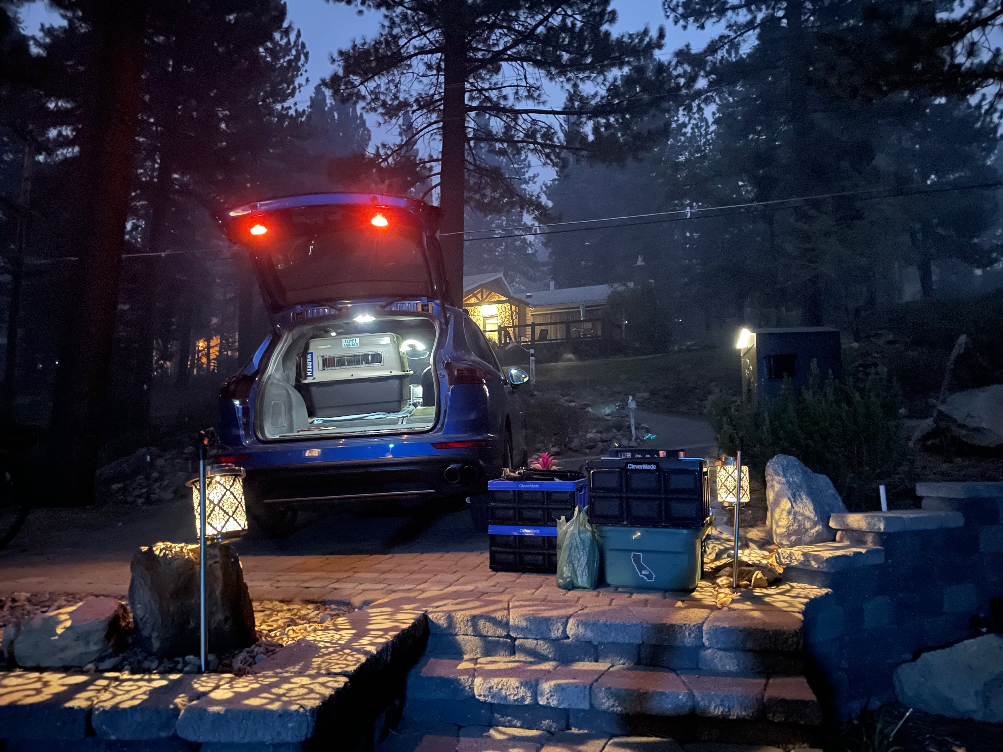 A blue car being packed with supplies in a driveway.