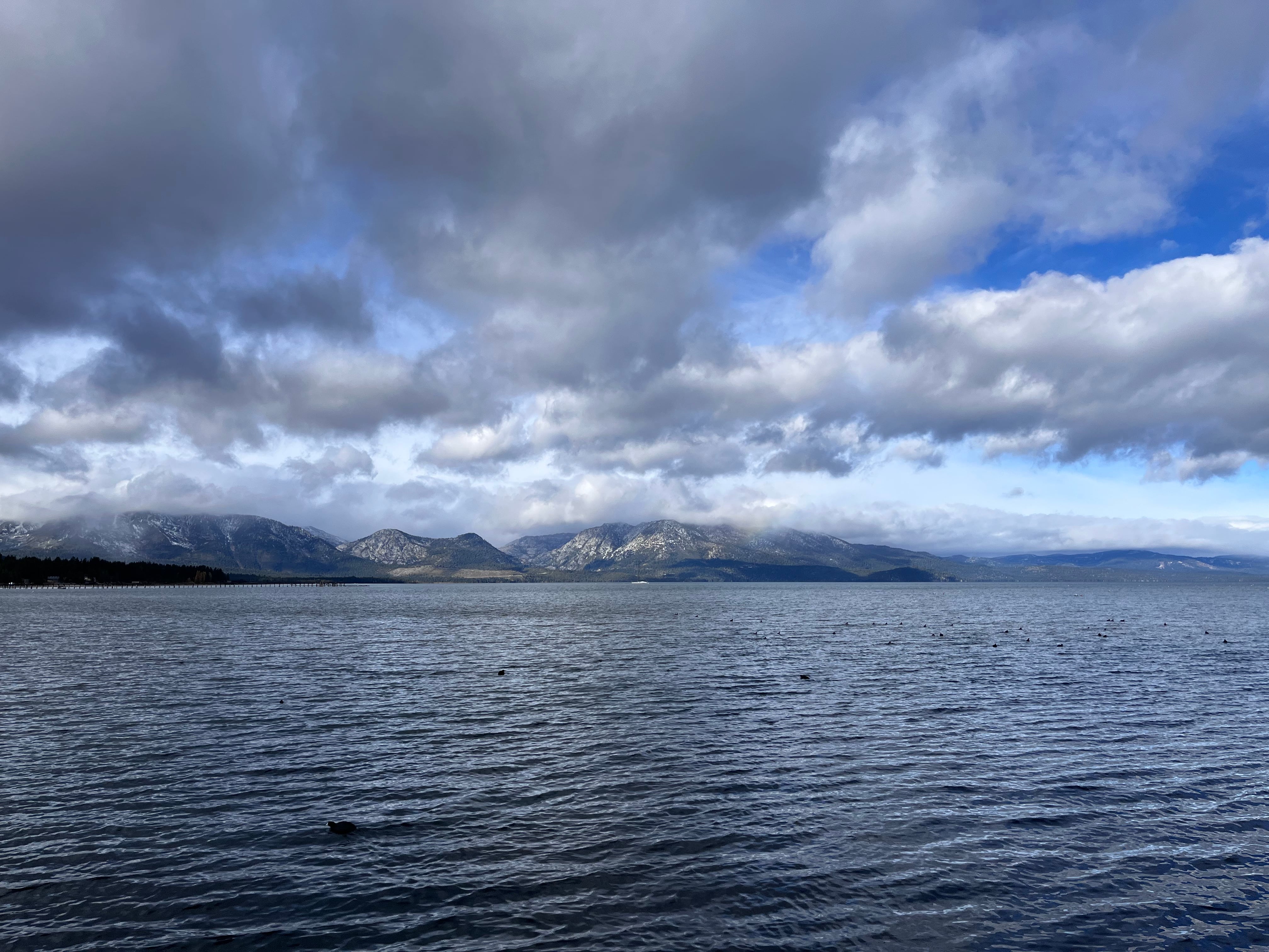 Photo taken from the middle of a lake. The sky is gray and partly cloudy, with mountains in the background.