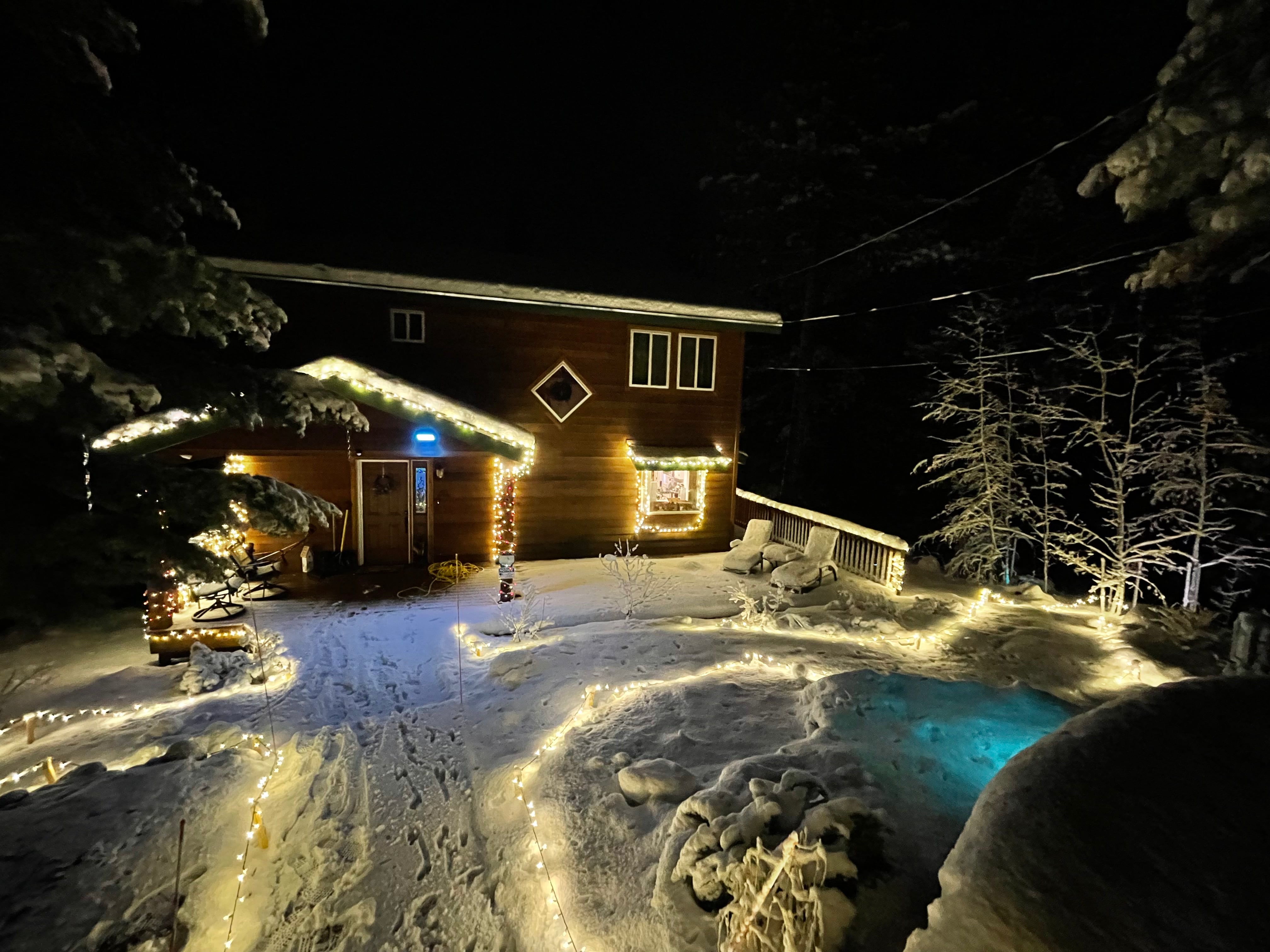 Photo of a house at night. Christmas lights outline walking paths and edges of the building.