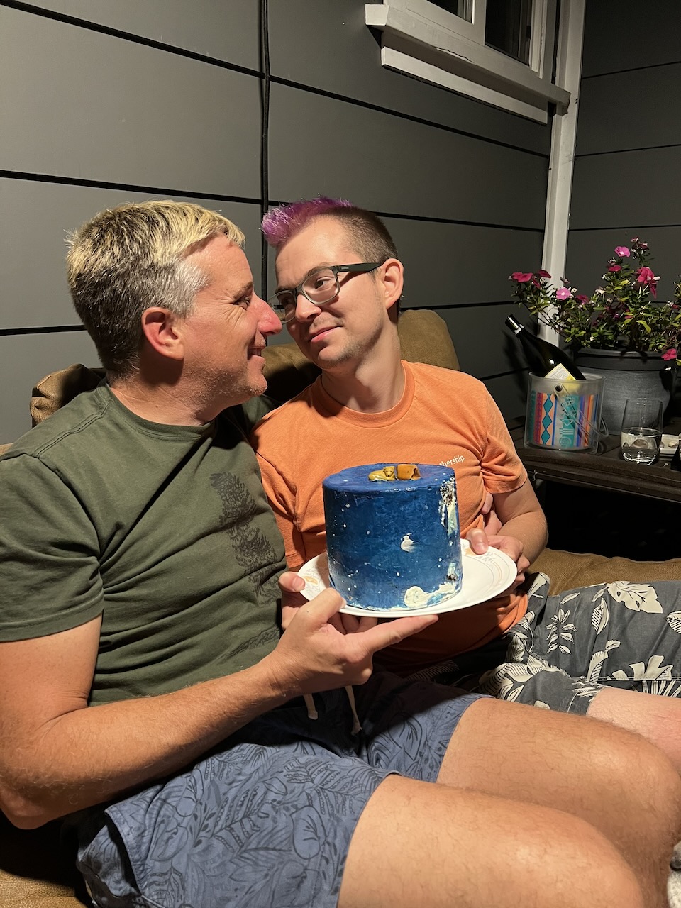 Myke and James sitting on a couch holding a small cake.