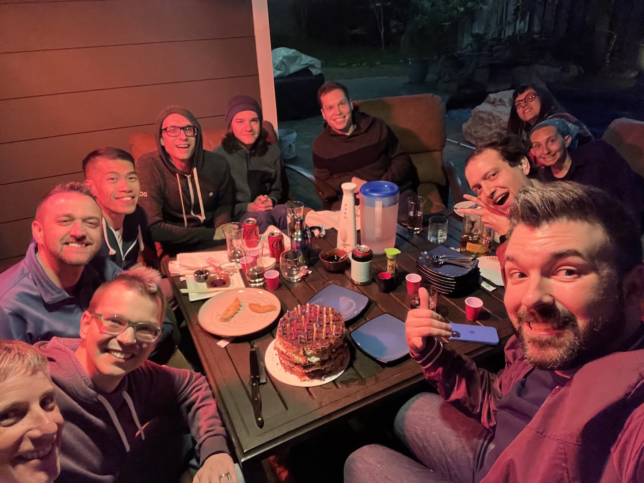 A group of people sitting around a table with a birthday cake and candles on it.