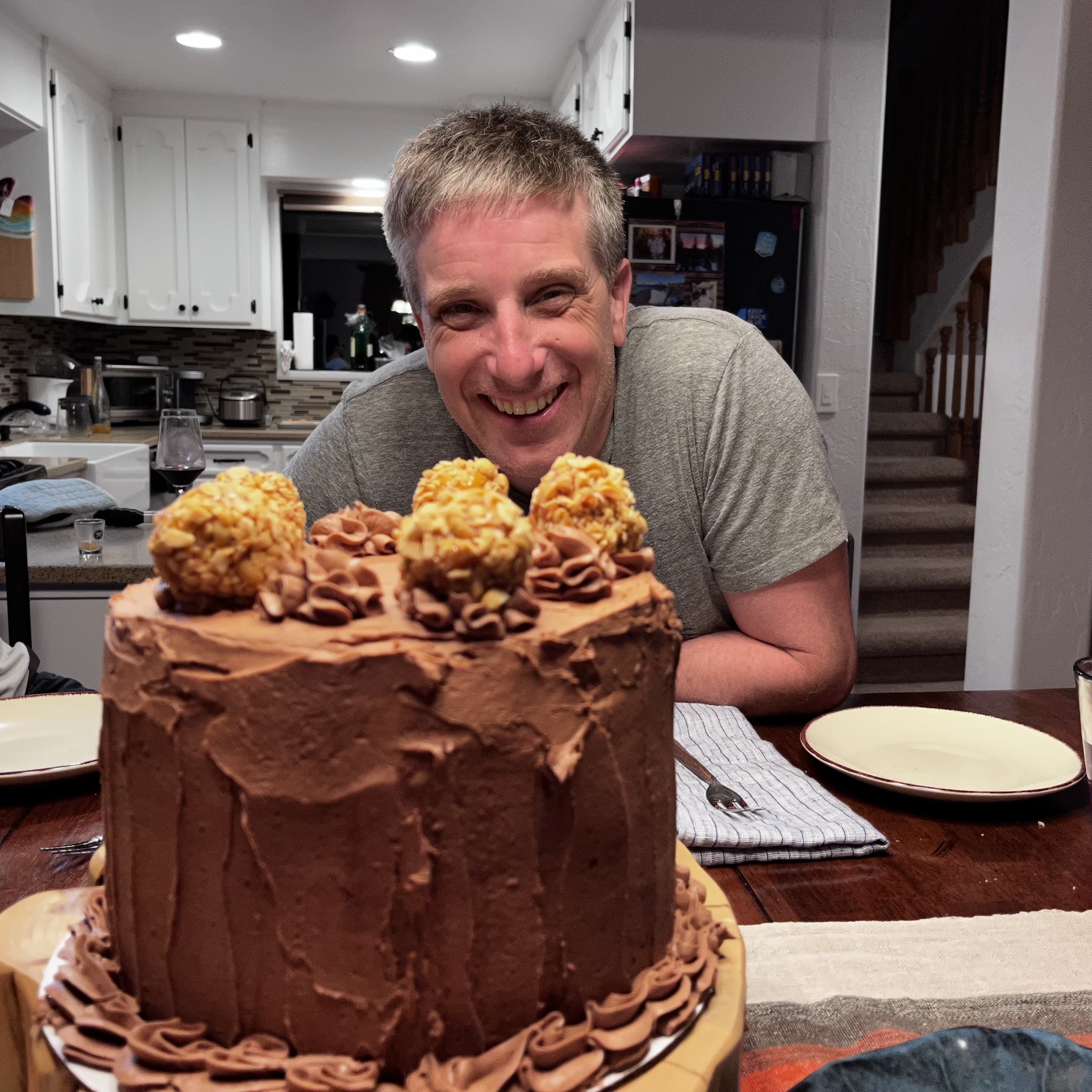 Myke sitting behind a large cake smiling.