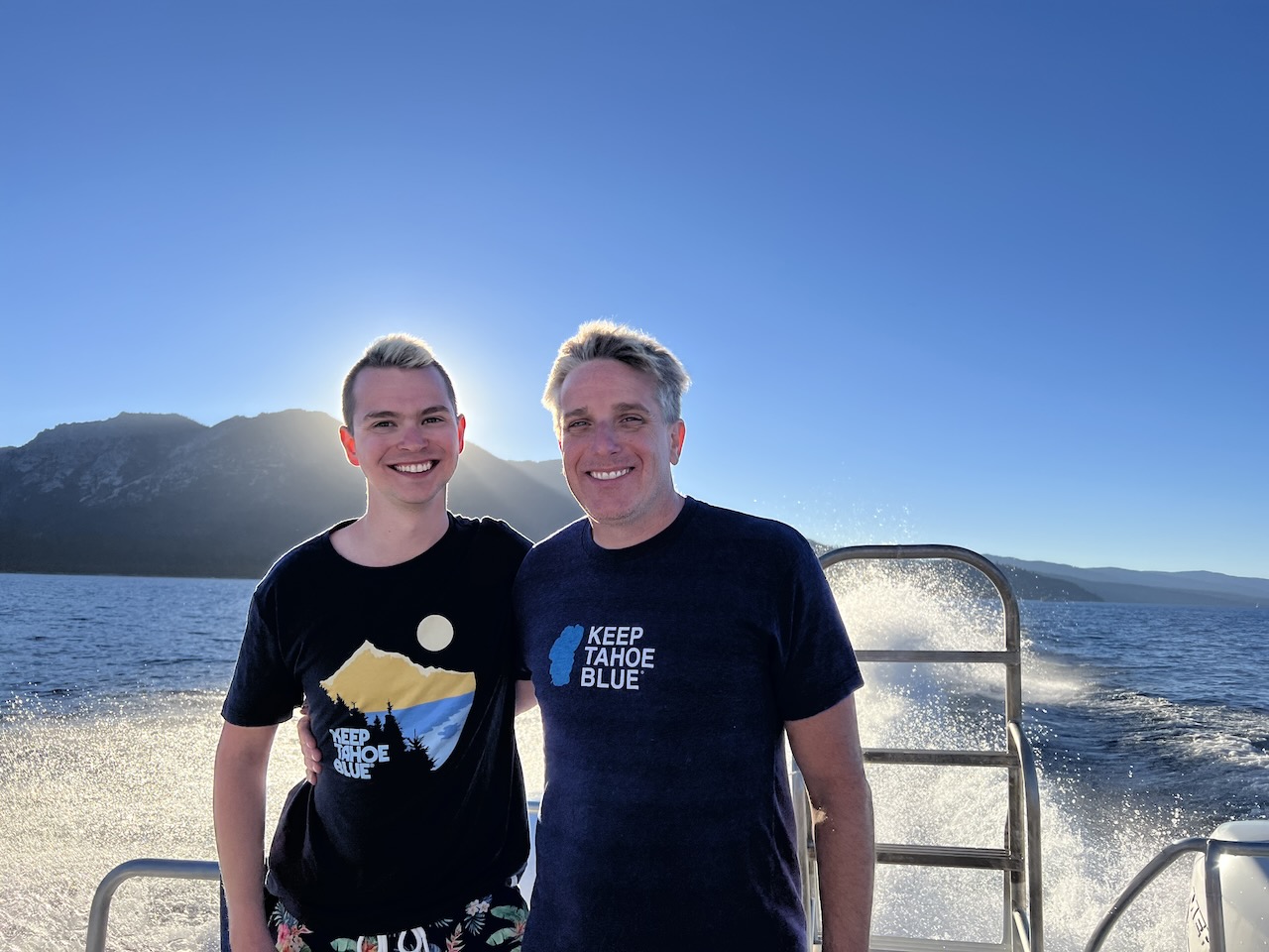 James and Myke standing on a boat with mountains in the background.