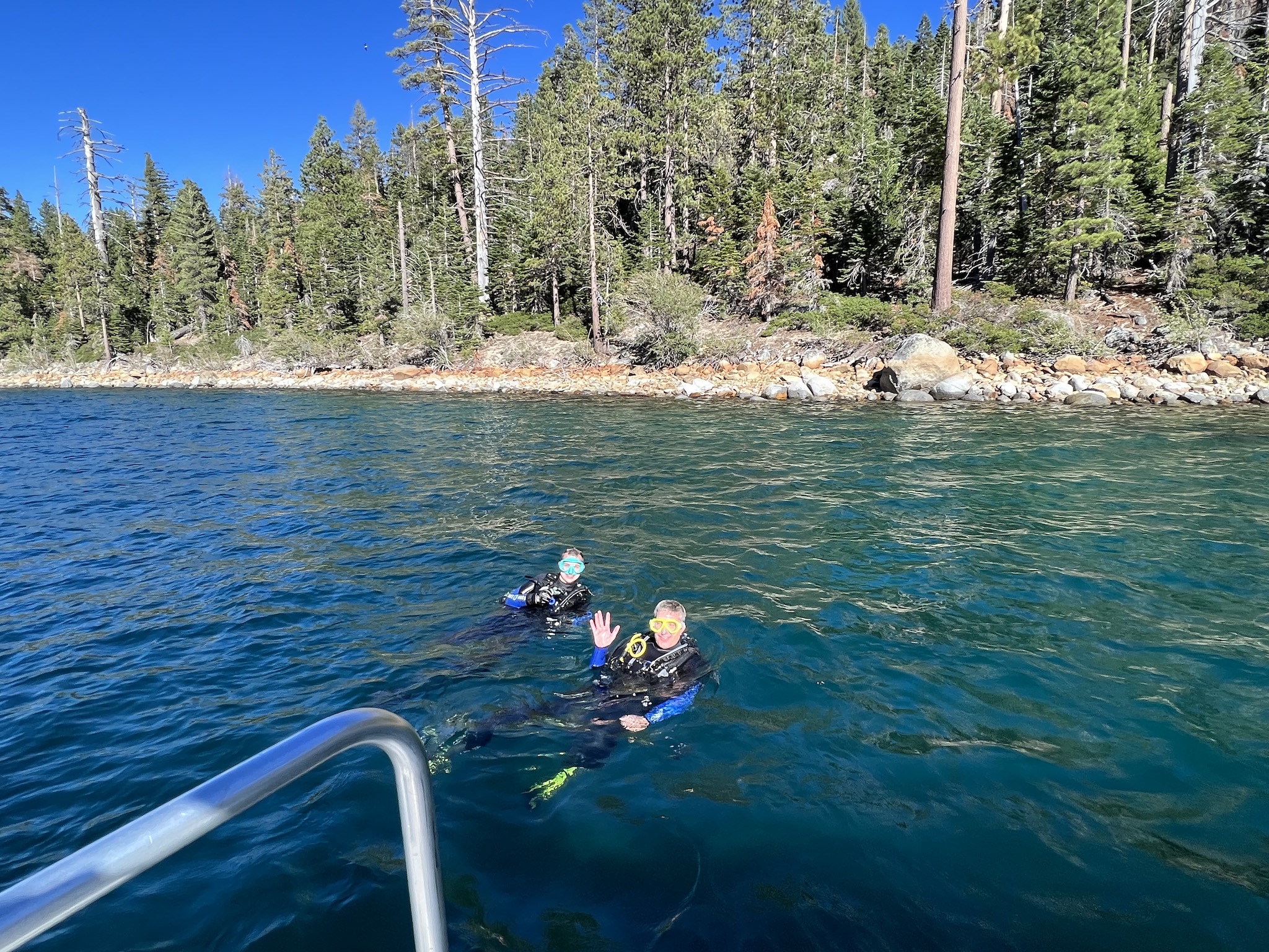 Myke and James floating in Lake Tahoe, trees and a shoreline are in the background.