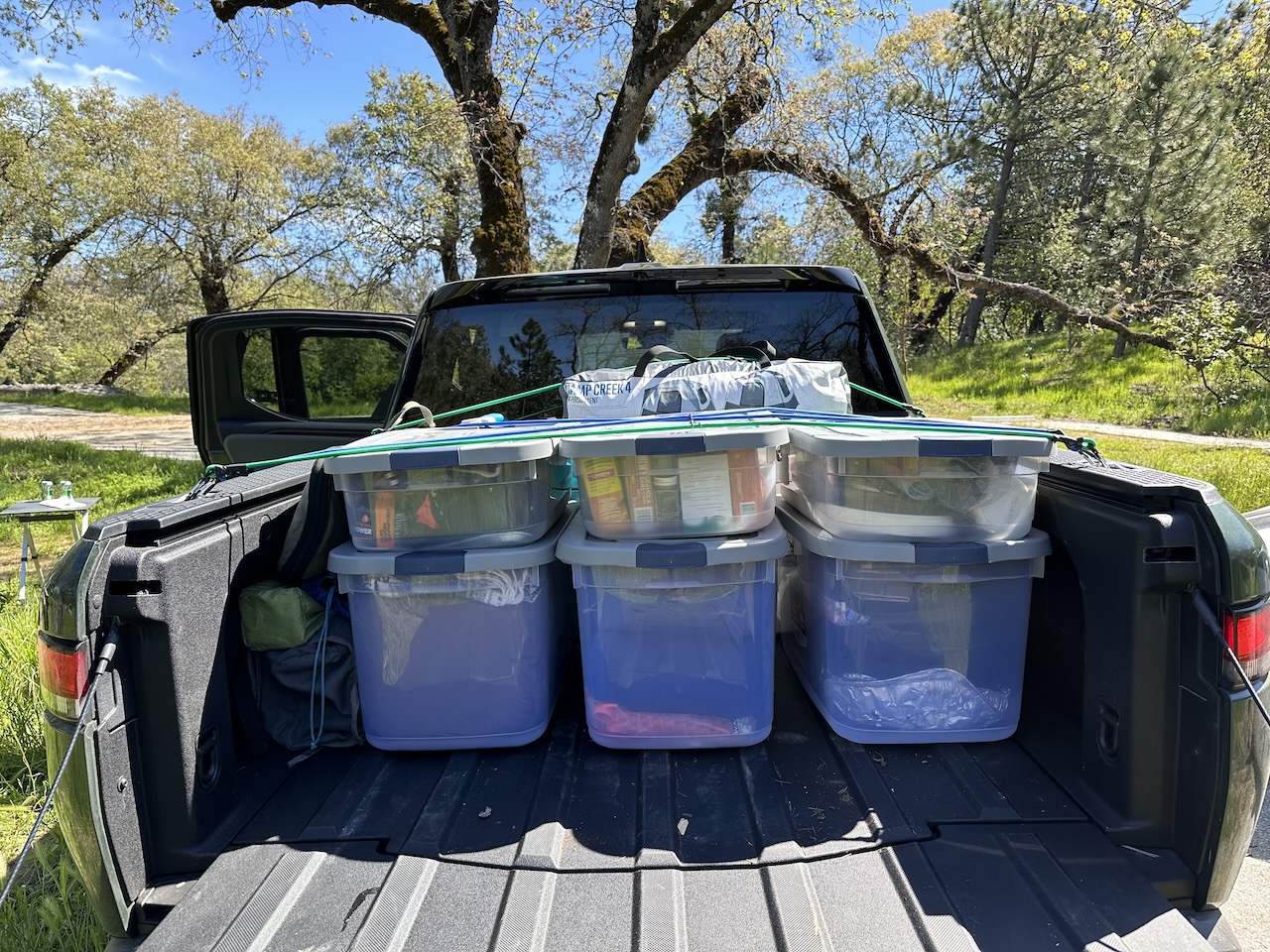 The back of a truck with six plastic totes strapped down by bungee cords.