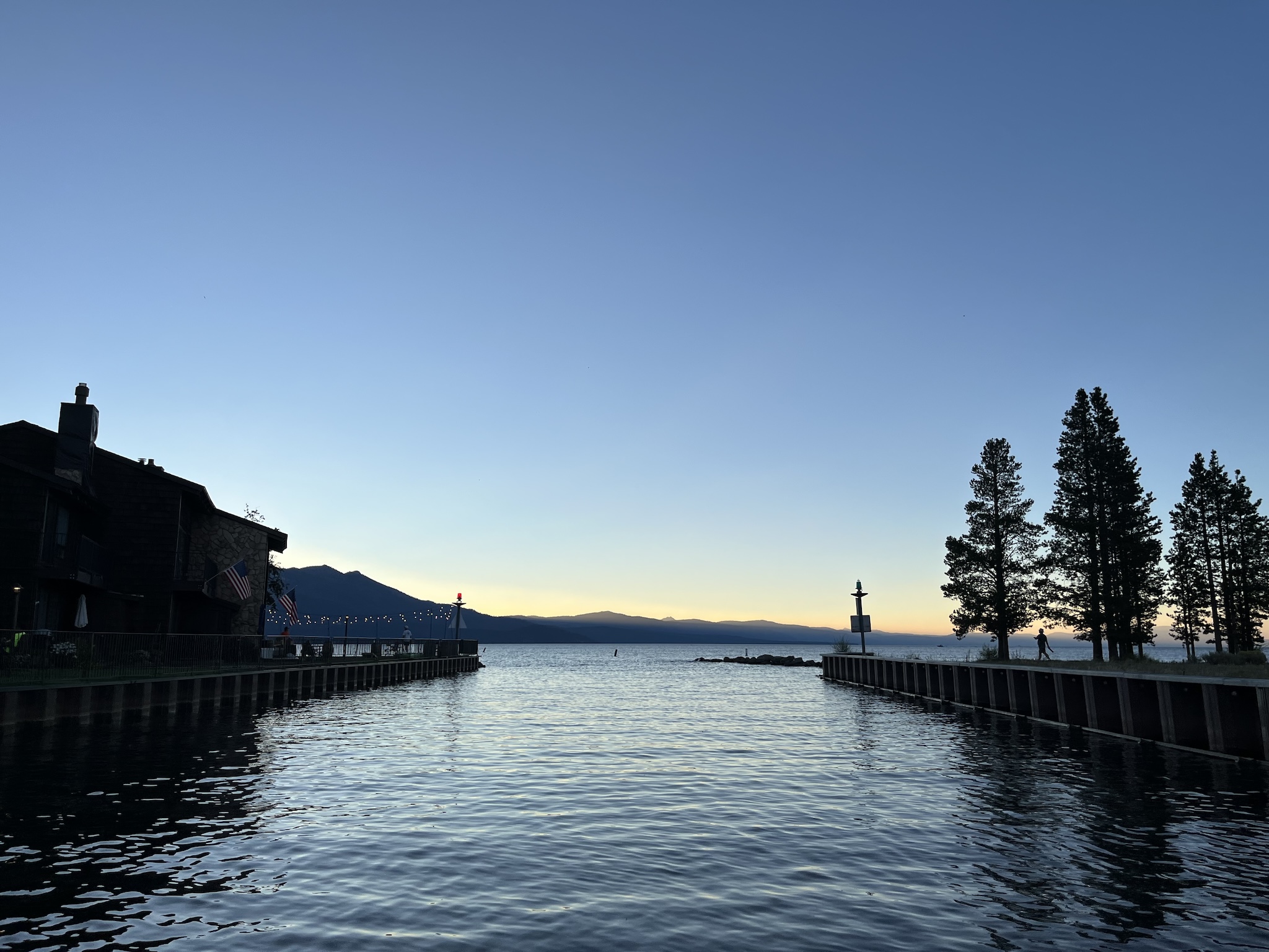 Man made channel, opening up into a large lake, with iron walls on either side. To the left are condos and on the right pine trees and a single person.