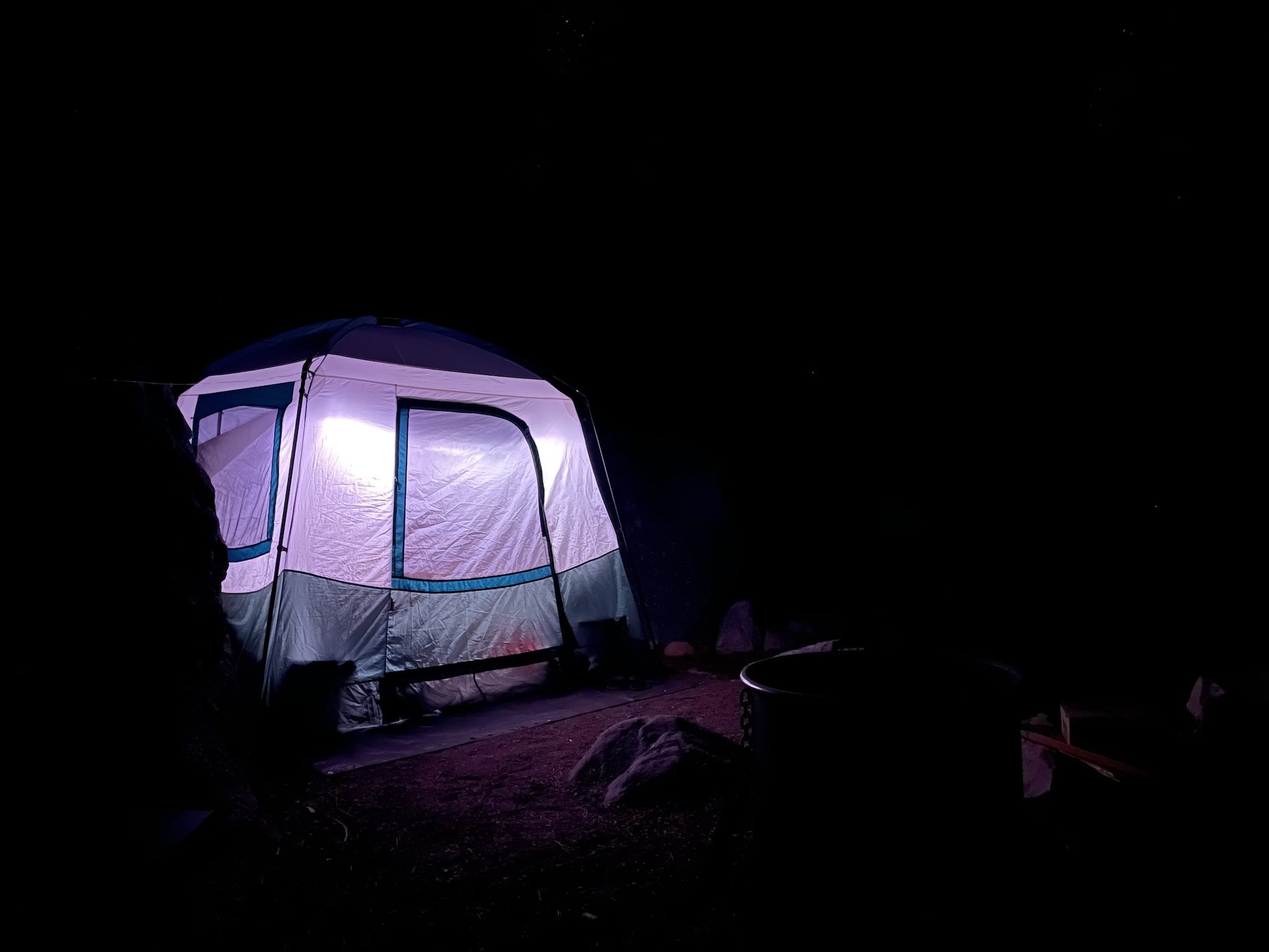 A tent, bright lit from the inside, in an otherwise black photo. A fire pit is just barely visible.