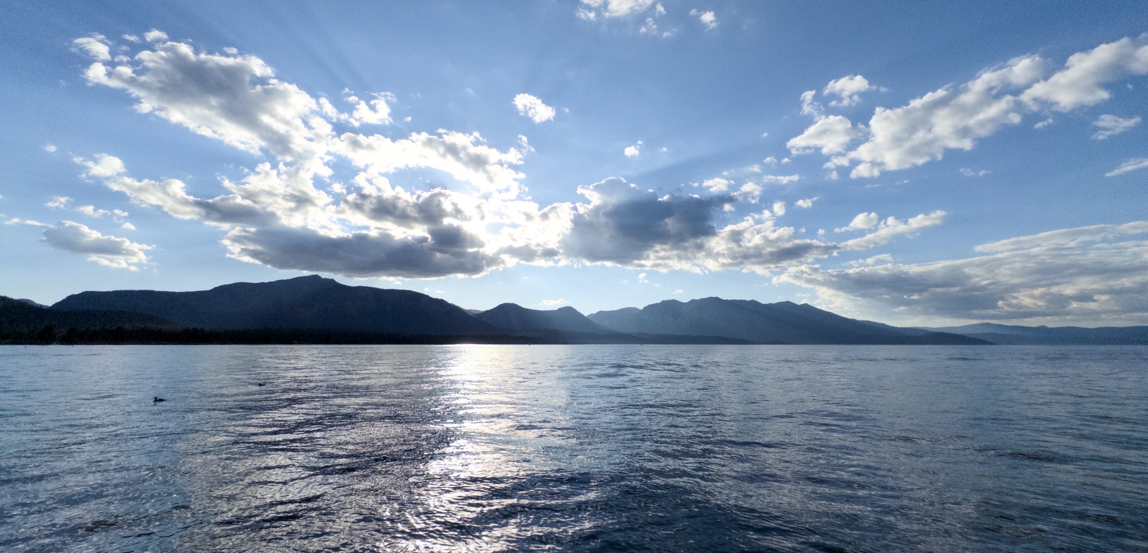 The sun, shining through partial cloud cover above two mountain peaks.