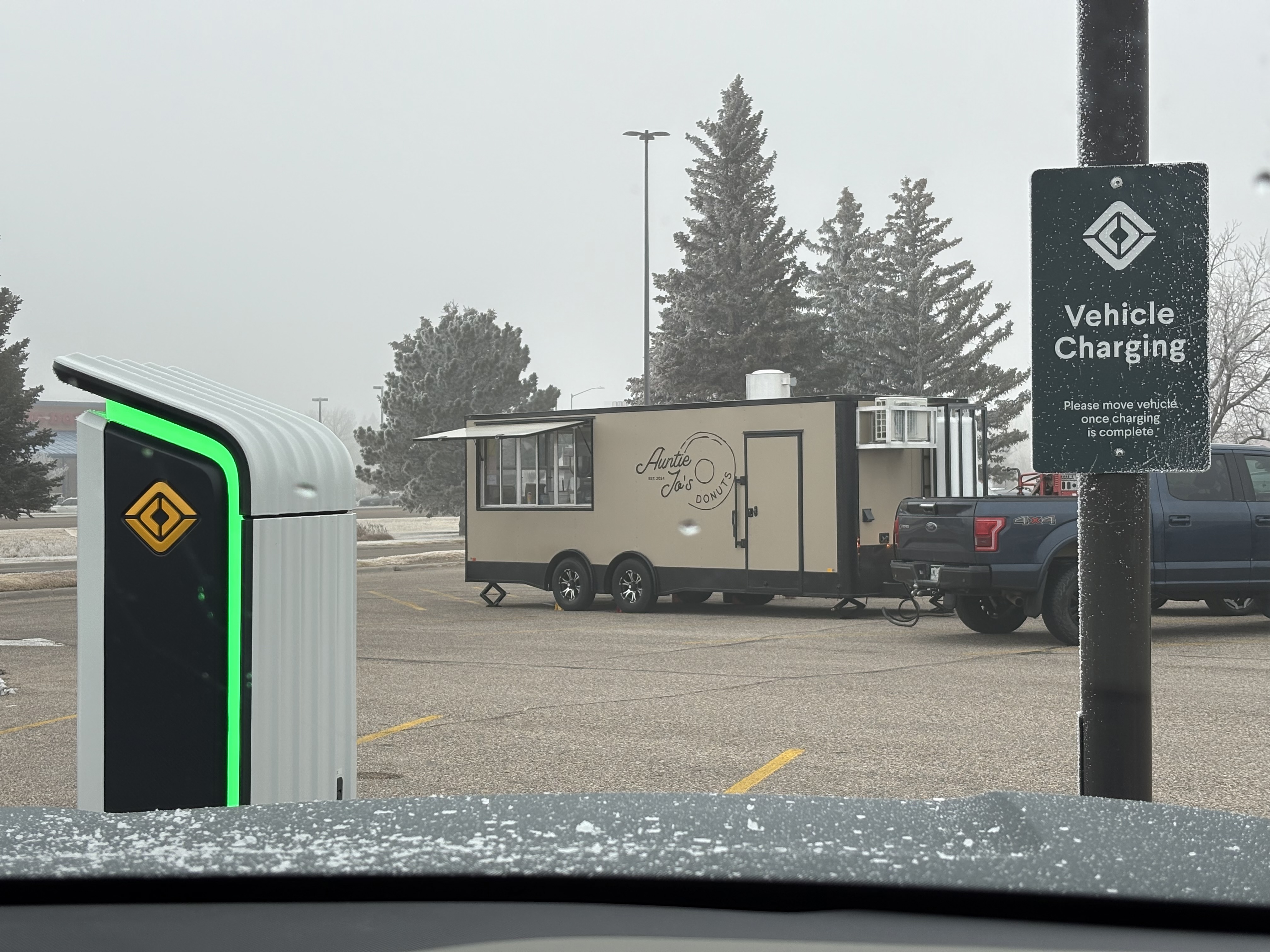 Food truck with a sign advertising Antie Jo's donuts on the side. A truck hood and EV charger are visible in the foreground.