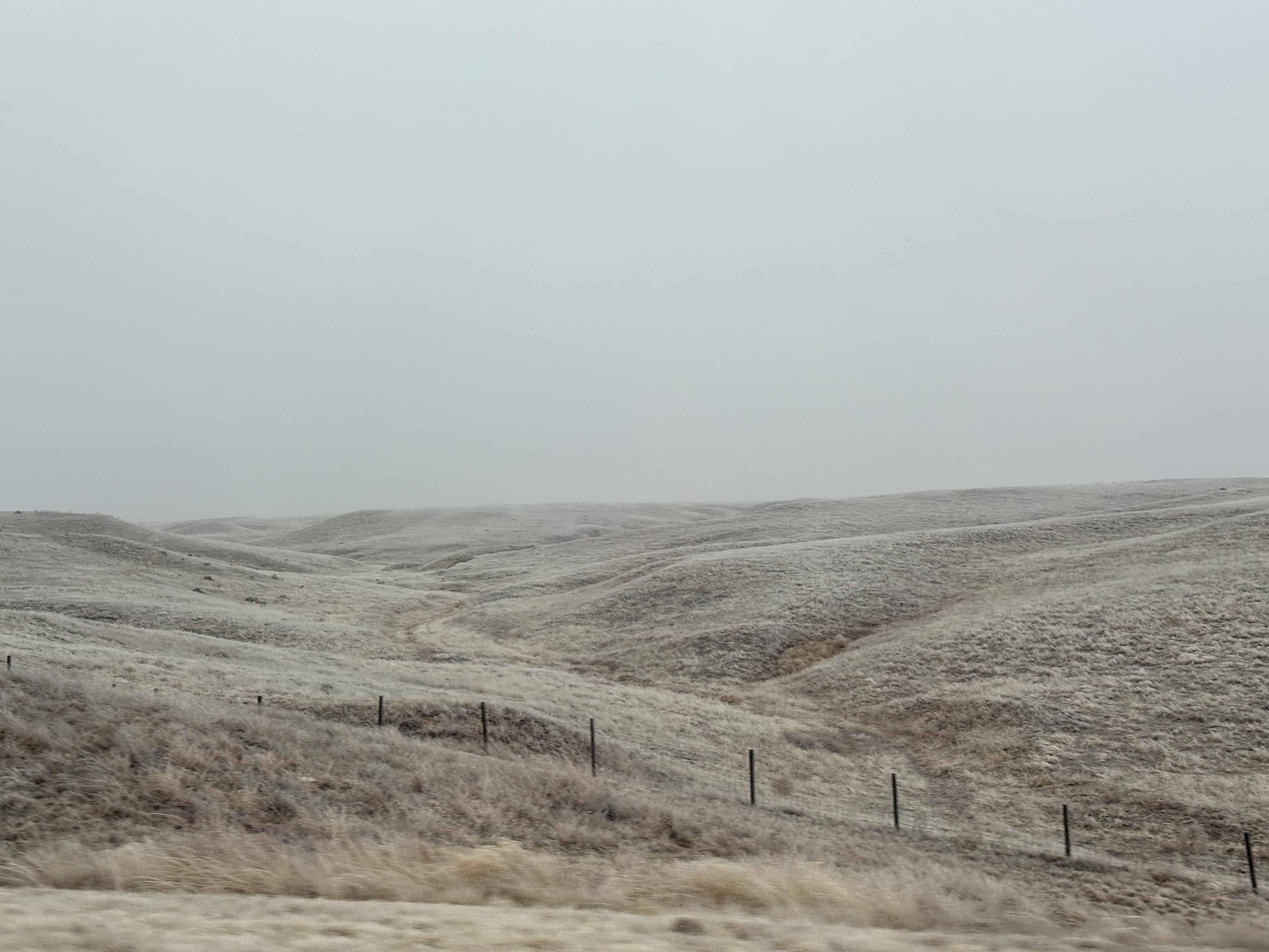 Barren hills with a small wire fence. Visibility is limited by fog.