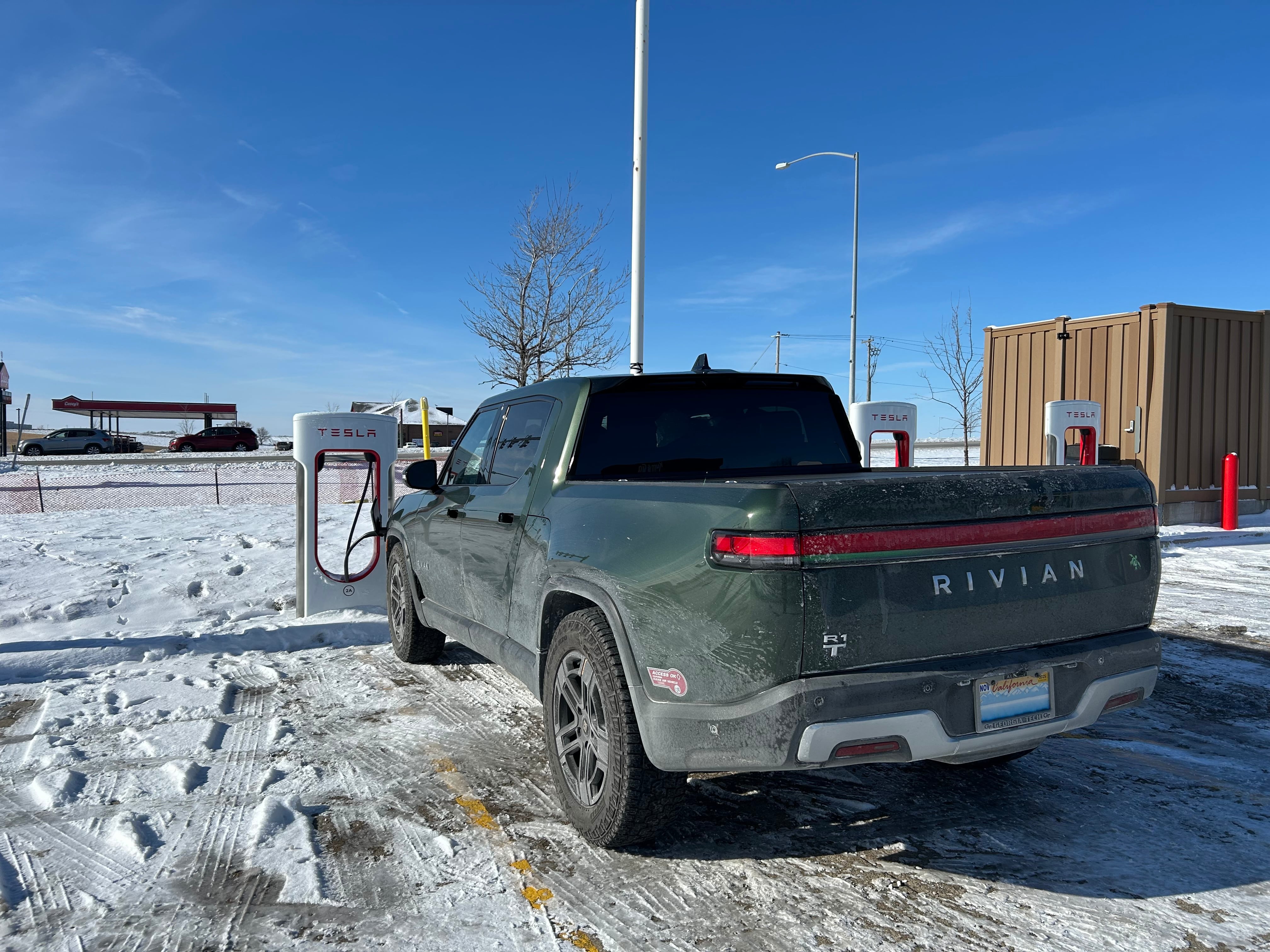 Rivian truck parked at a Tesla charging station. The parking lot is obscurd by a small layer of snow.